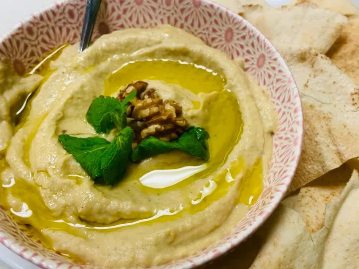 Hummus topped with olive oil, mint and a walnut, served beside flatbread.