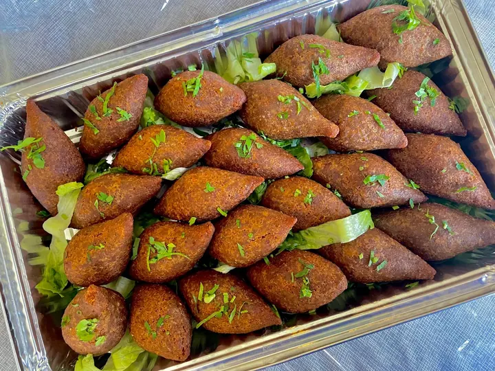 Golden-brown kibbeh arranged on lettuce in a catering tray and garnished with herbs.