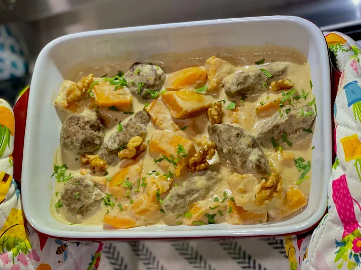 Pumpkin stew with ground beef in creamy tahini sauce, garnished with herbs and walnuts.