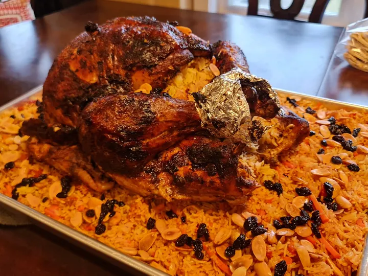 Whole roasted turkey served on a tray of rice with nuts and raisins.